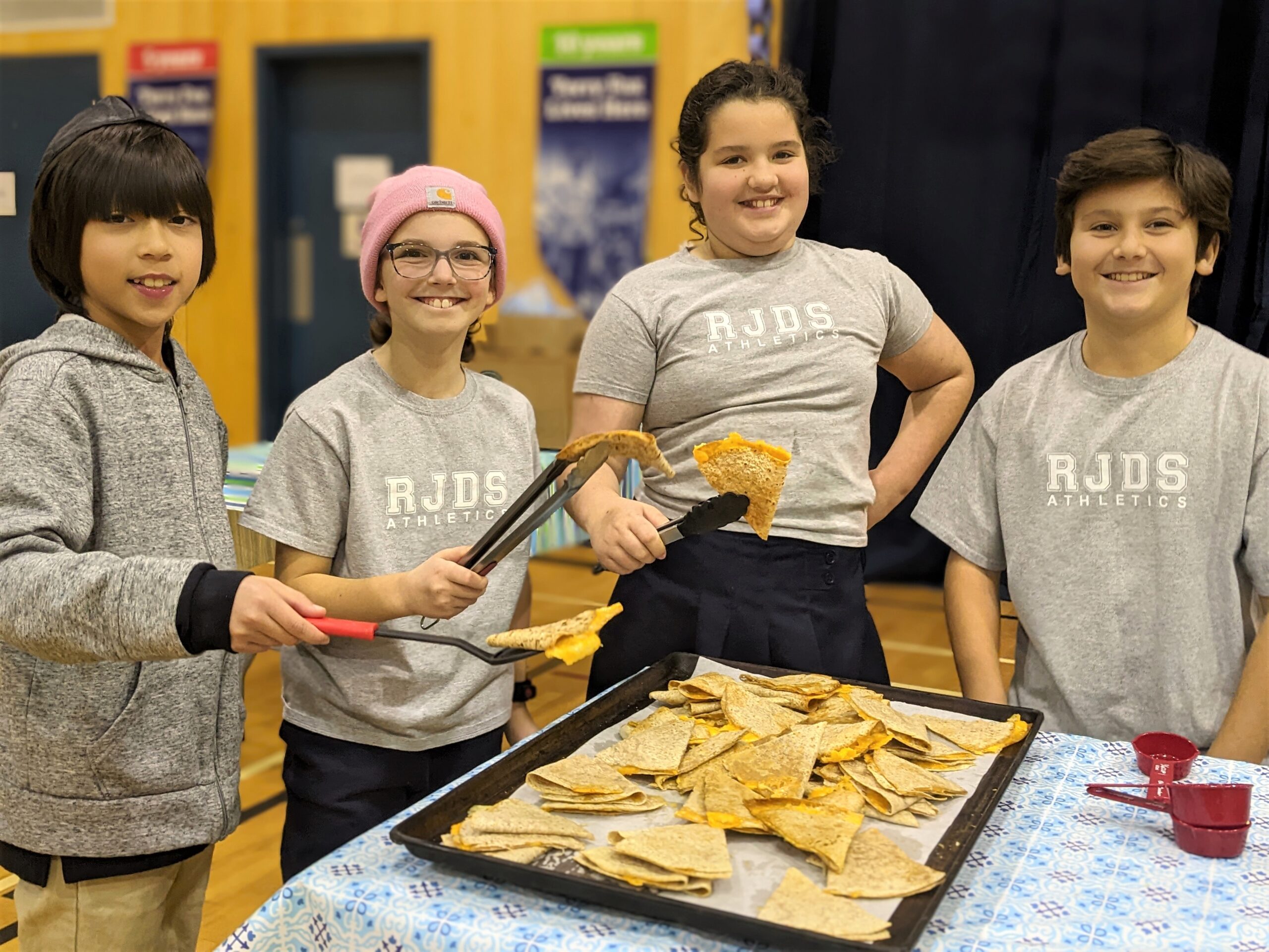 RJDS students smiling into the cameral while waiting to serve lunch to their schoolmates